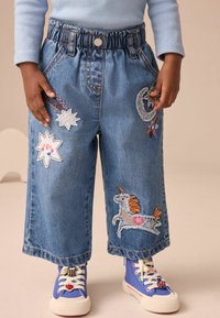 Pantaloni culotte in denim con cintura elastica. Presentano toppe ricamate colorate: un unicorno, stelle e motivi geometrici.