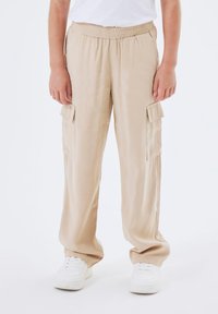 Beige cargo-byxor gjorda av lättviktsmaterial har en elastisk midja och sidofickor. Stylat med vita sneakers.