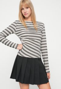 Sweter w paski w czerni i kremie, z prążkowaną fakturą i długimi rękawami, w połączeniu z czarną spódnicą plisowaną.