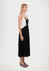 Czarna i biała, bezrękawnikowa sukienka z dekoltem w kształcie litery V, zwiewny materiał i dopasowana góra. Połączona z czarnymi sandałkami na obcasie.