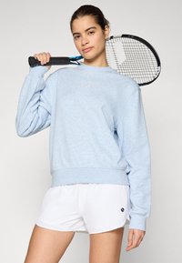 Light blue sweatshirt with ribbed cuffs and hem, featuring subtle white logo. Paired with white shorts, holding a black tennis racket.