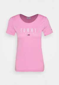 Różowa bawełniana koszulka z okrągłym dekoltem, z nazwą marki "TOMMY" i "JEANS" w białym kolorze, oraz małym kolorowym logo na rękawie.