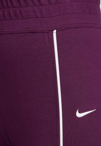 Pantalons de sport violets avec une texture lisse, dotés d'une bande latérale blanche et d'un petit logo Nike blanc sur le bas de la jambe.