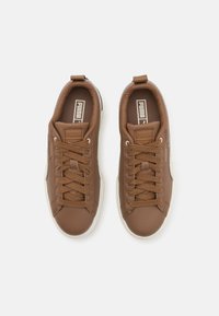 Sneaker in pelle marrone con tomaia testurizzata, punta tonda e suola in gomma bianca spessa. Presenta lacci a contrasto e dettagli del logo sulla linguetta.