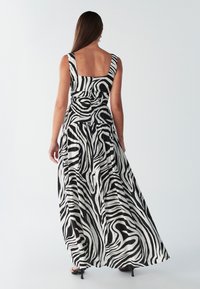 Abito lungo con stampa zebra in bianco e nero, caratterizzato da uno scollo quadrato, vita aderente e tessuto fluente. Motivo testurizzato su tutta la superficie.