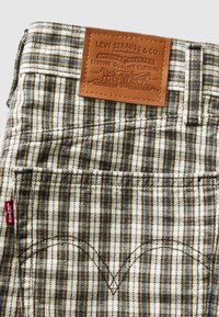 Poche arrière d'un jean Levi's à carreaux avec une étiquette en cuir marron Levi Strauss & Co. et une étiquette en tissu rouge Levi's sur la couture latérale.