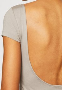 Světle šedý bodysuit s krátkými rukávy a hlubokým výstřihem na zádech. Tkanina vypadá hladce a má jemný lesk.