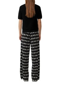 Suéter negro de manga corta con textura de canalé, combinado con pantalones plisados de lunares blancos y negros. Corte holgado, estilo de pierna ancha.