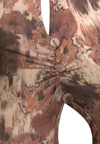 Gros plan sur un tissu avec un motif floral abstrait marron et rose, comprenant trois boutons recouverts de tissu et des coutures froncées.