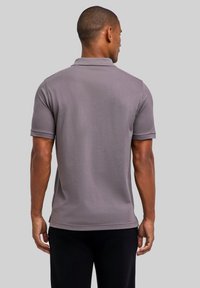 Szara koszulka polo z krótkimi rękawami, teksturowana tkanina i ostrym kołnierzykiem. Boczne rozcięcia u dołu, dopasowana sylwetka i minimalistyczny wzór.