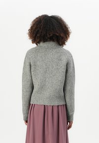 Maglione grigio a maglia con colletto alto e orlo a coste, caratterizzato da maniche lunghe e una finitura testurizzata. Indossato su una gonna rosa a pieghe.