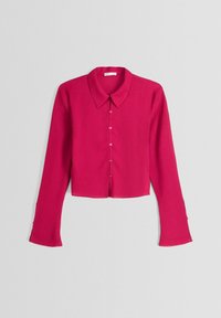 Camisa corta de fucsia con botones, cuello, mangas largas y una tela texturizada. Cuenta con botones en la parte delantera y puños de manga abiertos.
