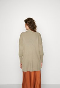 Lunga cardigan beige chiaro realizzata in tessuto a coste con una vestibilità rilassata e spalle abbassate, abbinata a una gonna maxi color ruggine.