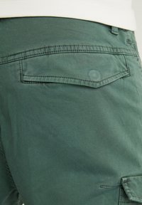Gröna bomullscargo-shorts med bakficka och flikdetalj, förstärkt sömnad och mjuk textur.