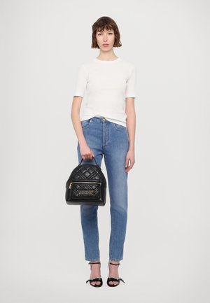 Černý prošívaný batoh z umělé kůže s přední kapsou na zip a zlatými detaily, v kombinaci s bílým upnutým topem a modrými rovnými džíny.