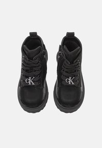 Czarne botki za kostkę z błyszczącym wykończeniem, z sznurowanym przodem i zamkiem błyskawicznym z boku, ozdobione srebrnym logo na języku.