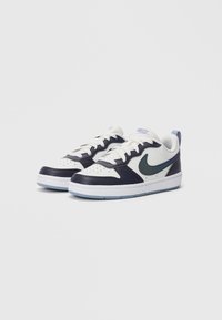 Adidași Nike cu un design joasă, albi și albastru închis, cu swoosh teal, șireturi albe și tălpi bleu deschis, așezați unul lângă altul pe un fundal simplu.