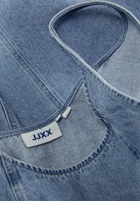 Tissu en denim bleu clair avec une texture lisse, doté d'un col rond et de l'étiquette "JJXX" brodée en bleu.