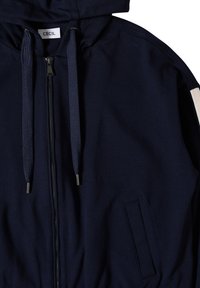 Veste à capuche marine avec fermeture éclair, dotée de cordons texturés, de poches latérales et d'une accentuation contrastante sur la manche.