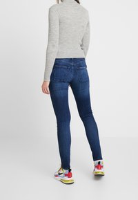 Jersey de cuello vuelto gris con textura acanalada, diseño ajustado; combinado con jeans ajustados azul oscuro que cuentan con bolsillos traseros; zapatillas multicolores con detalles.