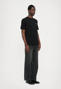 Tricou din bumbac negru cu mâneci scurte și guler rotund, asortat cu blugi largi gri închis, cu cusături laterale, și pantofi negri.