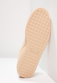 Suola beige di una scarpa Puma con un battistrada a stella appoggiata contro un angolo di muro bianco su un pavimento bianco.