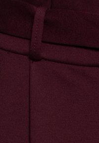 Burgundská tkanina s hladkou texturou, vybavená poutkem na pásek, plochým předním dílem a tvarovanými švy pro strukturovaný design.