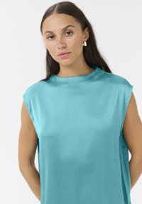 Haut sans manches turquoise en tissu soyeux et texturé, avec un col montant et une coupe décontractée, présentant de délicates rayures verticales.