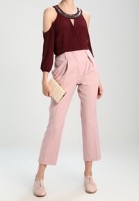Bordeaux kold-epaule skjorte med perlekant, parret med lyserøde højtaljede bukser og blush snørebåndssko. Accessories inkluderer en kremfarvet clutch.