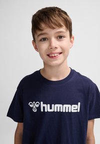 Tricou din bumbac de culoare bleumarin, cu un mare logo și grafică albă "hummel". Guler rotund și mâneci scurte, cu o croială relaxată.
