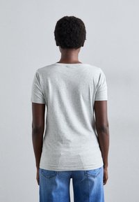 Tricou gri cu mânecă scurtă, fabricat din jerseu de bumbac, având guler rotund, textură netedă și croială lejeră, asortat cu blugi din denim albastru.