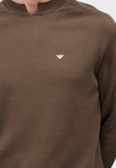 Καφέ πλεκτό πουλόβερ με μικρό λευκό κεντημένο λογότυπο στην αριστερή πλευρά του στήθους και ριμπ γιακά με μικρή εγκοπή.