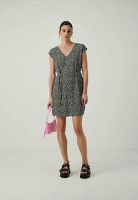 Melna kleita ar baltu ziedu rakstu, īsām piedurknēm, cinčotu vidukli un garumu virs ceļgaliem. Apvienota ar rozā rokassomu un masīvām sandālēm.