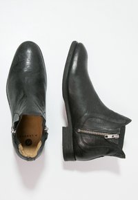 Mustan nahka ankle-bootit, joissa on tekstuuripinta, kaareva muoto, sivu vetoketju ja matala pinoalakorko. Sisäosa on vaalea ruskea ja siinä on brändäys.