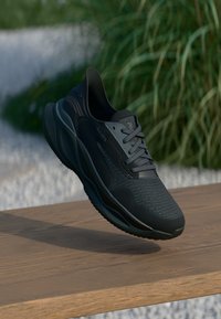 Baskets de sport noires avec dessus texturé et lacets reposant sur le bord d'une surface en bois à l'extérieur avec un arrière-plan de verdure floue.