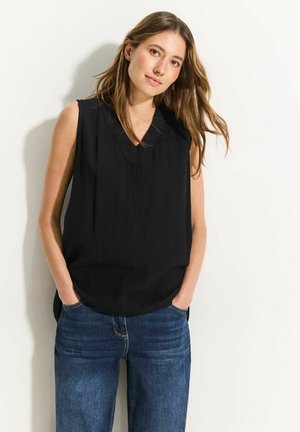 Top nero senza maniche con scollatura a V e tessuto testurizzato, abbinato a jeans larghi blu. Il top ha una vestibilità ampia e spacchi laterali.