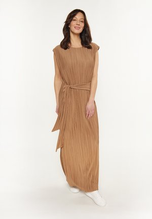 Beige plissiertes Maxikleid mit Kurzärmeln, tailliertem Schnitt und einem gebundenen Gürtel. Tragen mit weißen Sneakers vor einem neutralen Hintergrund.