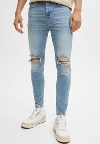 Ljusblå skinny jeans med slitna områden vid knäna, fransad fåll och subtil blekning. Matchat med vita sneakers.