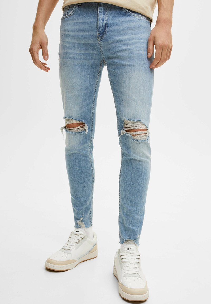 Ljusblå skinny jeans med slitna områden vid knäna, fransad fåll och subtil blekning. Matchat med vita sneakers.