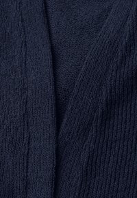 Nærbillede af mørkeblåt strikket stof, der viser detaljerede teksturerede mønstre og rib.