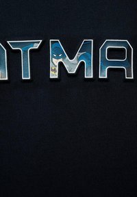 Camicia in cotone nera con grande scritta "BATMAN" in lettere contornate, con un grafico di Batman incorporato nelle lettere "A" e "M".