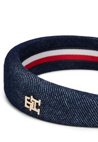 Bandă de cap din denim de culoare albastră închisă, cu un logo din metal aurit. Detalii interioare cu dungi roșii, albe și albastre. Textură moale și formă circulară.