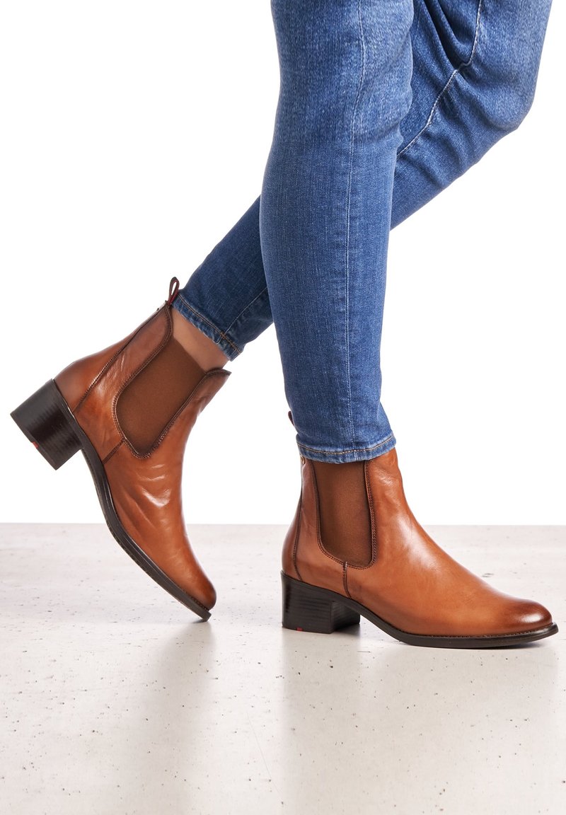 Bottes basses en cuir marron à finition polie, avec des panneaux latéraux élastiques et un petit talon bloc, portées avec un jean skinny bleu.