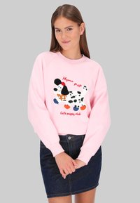 Sudadera rosa con un gráfico texturizado de un perro con detalles coloridos y el texto "Club de cachorros lindos." Se lleva con una falda vaquera.