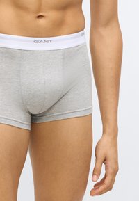 Les boxers en coton gris disposent d'une ceinture élastique blanche avec le logo « GANT ». Le tissu présente une texture douce et une coupe ajustée.