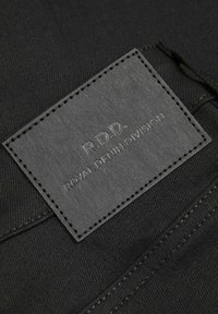Juodas džinsinis audinys su tekstūriniu odiniu užtrauktuku, pažymėtu "R.D.D. ROYAL DENIM DIVISION", su reljefiniu tekstu ir kontrastingais siūlais.