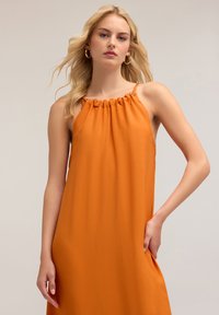 Vestido naranja sin mangas con un escote fruncido y tirantes delgados, que presenta un corte holgado y bolsillos laterales. Tejido suave y ligero.