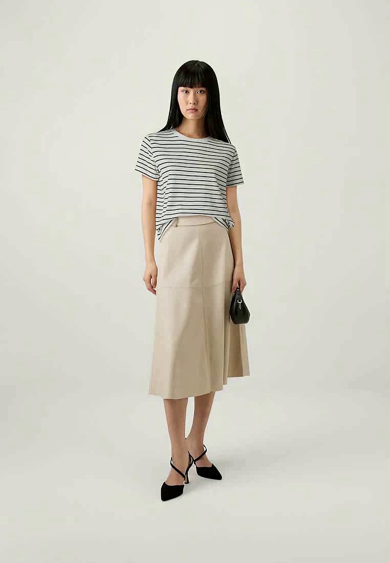 Femme portant un t-shirt à rayures noir et blanc, une jupe midi beige, des escarpins noirs à talons pointus, et tenant un petit sac à main noir.
