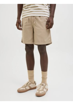 Bermudas beige con cintura ajustable, que presentan aberturas laterales y una tela suave. Combinadas con zapatillas beige y calcetines a juego. Camisa a rayas en la parte superior.