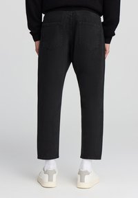 Pantaloni in denim nero con vestibilità rilassata, caratterizzati da una vita alta, design a cinque tasche e dettagli di cucitura delicati. Indossati con scarpe bianche.